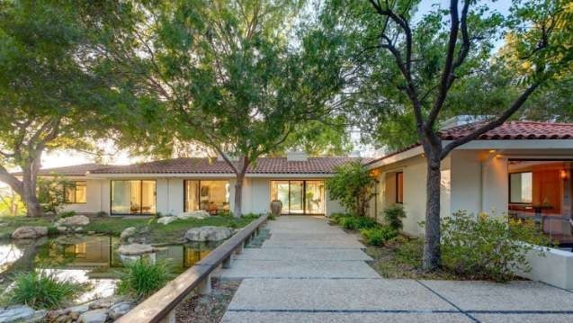 Rashida Jones house with a grey stone tiled pathway with green trees and a small pond on the side